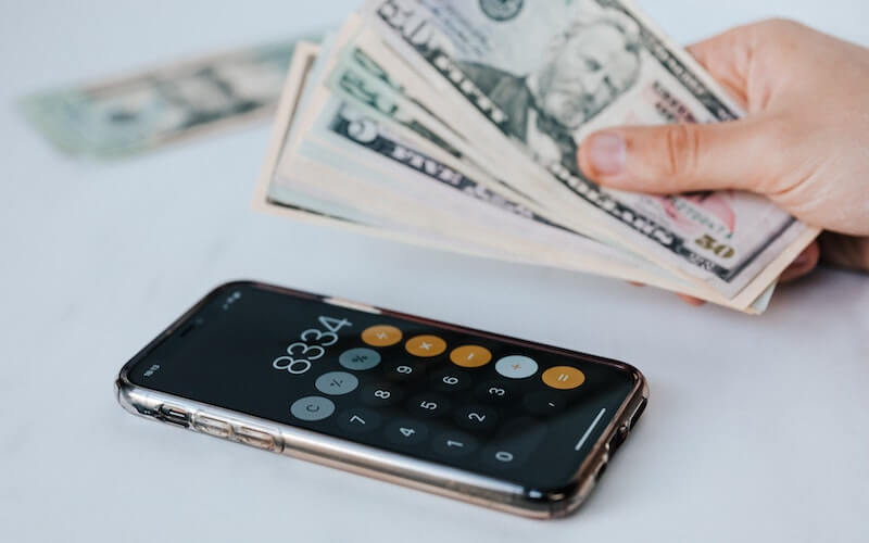 person counting money and using phone calculator